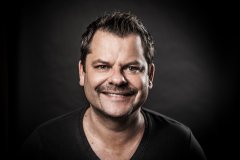 Bild zeigt ein Portrait-Foto von Ingo Appelt vor einem dunklen Hintergrund