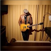 Bild zeigt Henrik Freischlader mit Gitarre vor einem beige gelben Vorhang