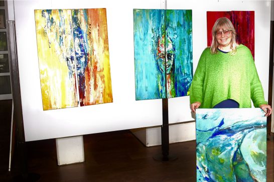 Arnhild Koppel neben 2 ihrer Bilder wärend sie ein 3. in den Händen hält