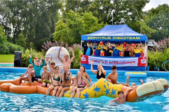 Einige Kinder die auf einem Aufgeblasenen Gegenstandt in einem Pool sitzen. Im Hintergrund am Poolrand ist das DiscoTeam Zephyrus zu sehen.